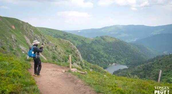 Un randonneur prend une photo du lac depuis un sentier escarpé dans les Vosges.