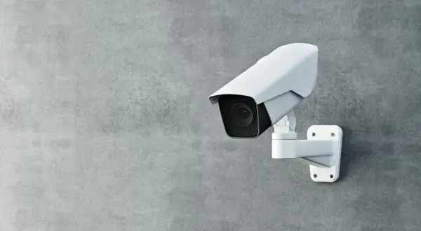 Une caméra de surveillance blanche est fixée sur un mur de béton. Cette caméra sans internet assure une sécurité discrète.
