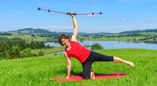 Frau macht Yoga mit einem Schwingstab, dem Testsieger für Balance-Training, vor malerischer Alpenkulisse.