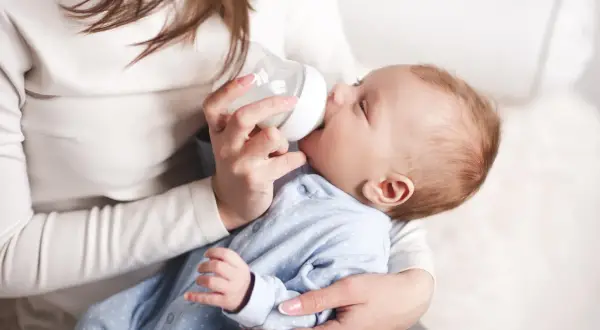 Matka karmi dziecko butelką. Uważaj na przekarmienie niemowlaka mlekiem modyfikowanym objawy, by uniknąć problemów.