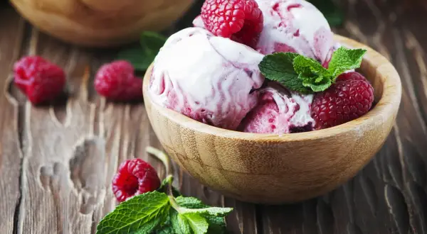 Pyszny sorbet malinowy w drewnianej miseczce, ozdobiony świeżymi malinami i miętą. Idealny deser, jak zrobić sorbet malinowy.