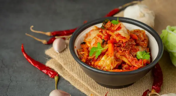 Miseczka z pikantnym kimchi, obok papryczki chili i czosnek. Idealne składniki, by dowiedzieć się, jak zrobić kimchi.