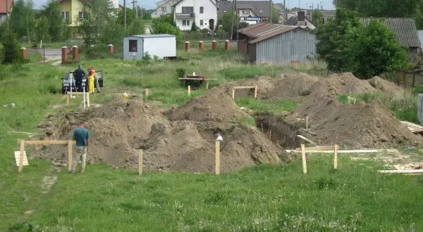Prace ziemne pod budowę domu. Kopanie fundamentów, hałdy ziemi i pracownicy. Zastanawiasz się, ile kosztuje wykopanie fundamentów pod dom?