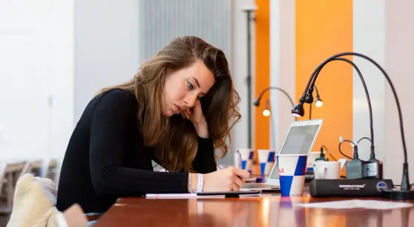 Młoda kobieta pochylona nad notatkami, szukająca sposobów, jak się lepiej uczyć. Obok laptop i kubek z logo Red Bull.