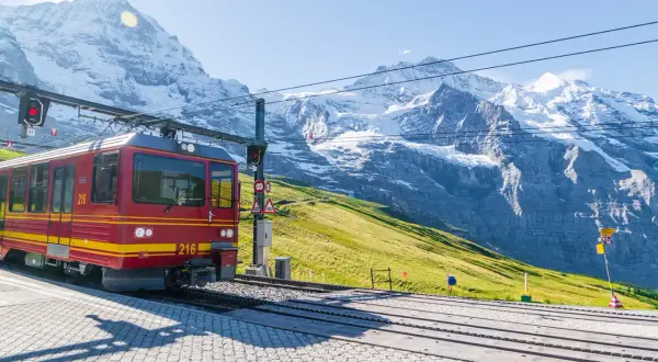 Treno rosso in montagna, pronto a salire tra vette innevate e verdi pendii.