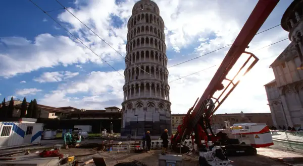 La Torre di Pisa prima e dopo i lavori di consolidamento: un cantiere con macchinari e operai accanto alla torre pendente.
