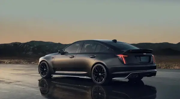 Mroczny Cadillac CT5 z czarnymi felgami i spojlerem na tle górskiego krajobrazu o zachodzie słońca.