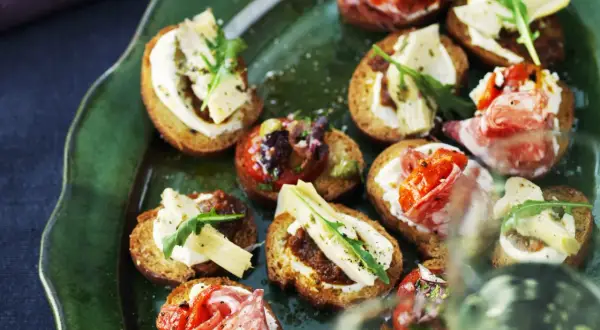 En grön tallrik med olika crostini topping: salami, tomat, ost och ruccola.