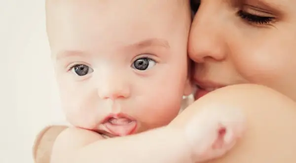 Zbliżenie na twarz niemowlaka z wyciągniętym językiem, przytulonego do matki.
