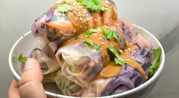 Kolorowe spring rolls z warzywami, polane kremowym sosem orzechowym i posypane orzeszkami. Idealne na lekki posiłek.