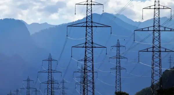 Linie energetyczne na tle gór. Wiele słupów wysokiego napięcia tworzy sieć, która może być wykorzystana w taryfie c12a godziny.