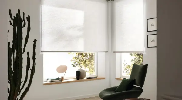 Moderne Sichtschutz-Fenster-Innen-Ideen: Helle Rollos mit dezentem Muster schaffen Privatsphäre und lassen Licht herein. Ein grüner Sessel lädt zum Entspannen ein.