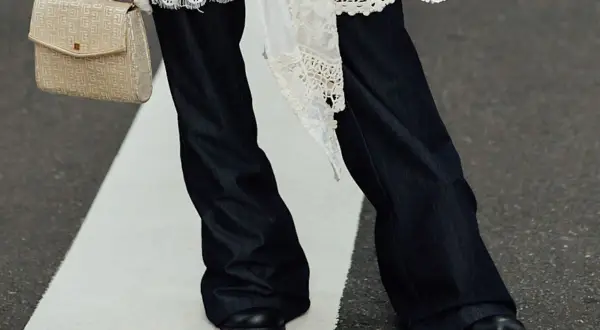 Eleganckie połączenie sukienki ze spodniami. Długie, ciemne dżinsy i biała, koronkowa narzutka tworzą stylowy look.