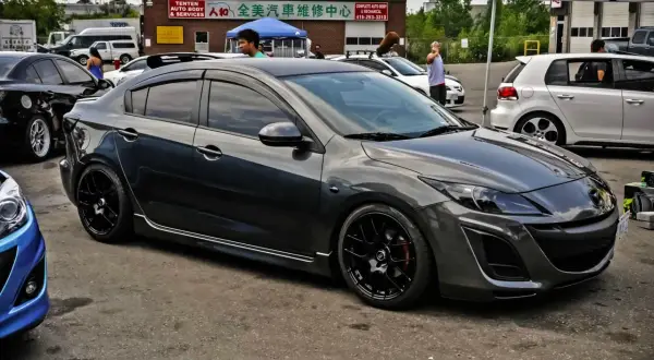 Mörkgrå Mazda 3 med svarta fälgar, redo för en tur. Kanske ett litet **Mazda 3 problem** med däcken?