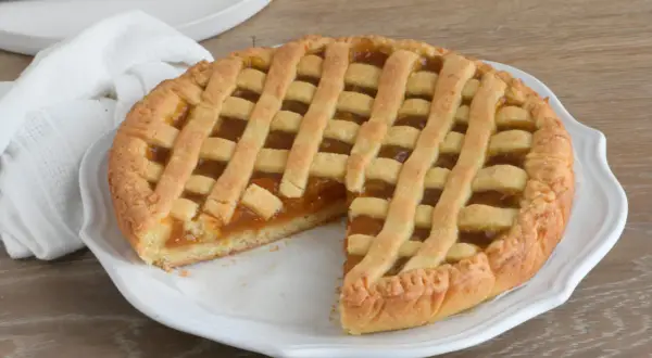 Crostata con marmellata, un classico della crostata ricetta tradizionale, servita su un piatto bianco con un tovagliolo di lino.