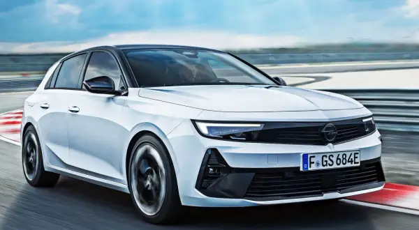 Biały Opel Astra GSe pędzi po torze wyścigowym, z kołami w ruchu, na tle błękitnego nieba.