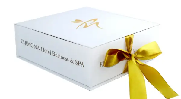 Eleganckie białe pudełko z logo Farmona Hotel Business & SPA, przewiązane złotą wstążką. Idealne na bon do spa.