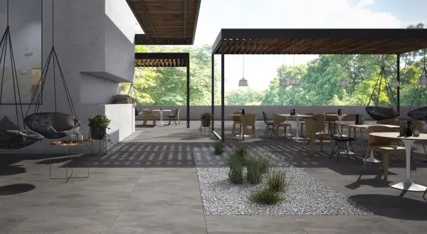 Spazio esterno moderno con tavoli, sedie e altalene, pavimentato con eleganti mattonelle per esterni grigie.