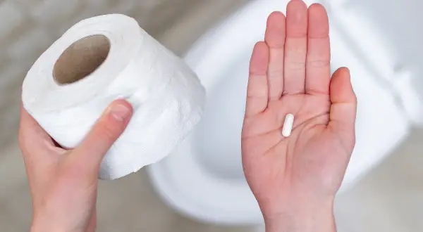 Mano con rotolo carta igienica e capsula bianca, possibile antibiotico per diarrea capre.