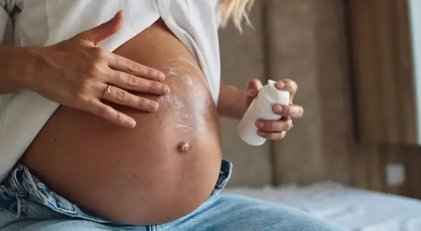 Manos aplicando crema en el vientre de una mujer embarazada. La crema, con un toque de rosa mosqueta, ayuda a cuidar la piel.