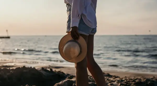 Sonnenuntergang am Kolberg Strand. Eine Frau hält einen Strohhut, während sie am Wasser entlang spaziert.