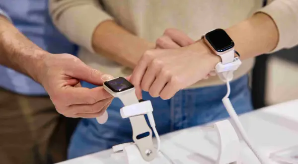Un homme montre comment charger une montre connectée à une femme. La montre est fixée à un support de démonstration.