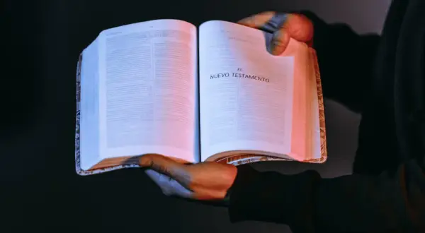 Otwarta księga z napisem "El Nuevo Testamento". W rękach trzymających ją można rozpoznać autor dziejów apostolskich.