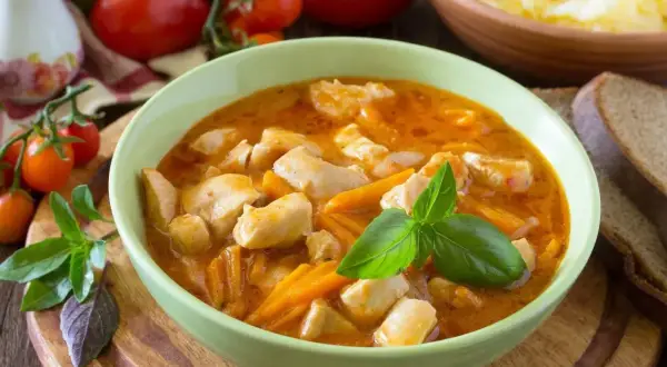 Aksamitny gulasz z piersi kurczaka z marchewką, udekorowany bazylią. Obok kromki chleba i miska purée ziemniaczanego.