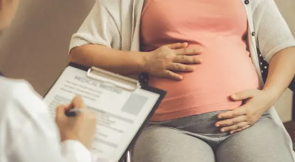 Lekarz notuje dane pacjentki, która trzyma dłoń na brzuchu. Obliczenia terminu porodu opierają się na regule Naegelego.