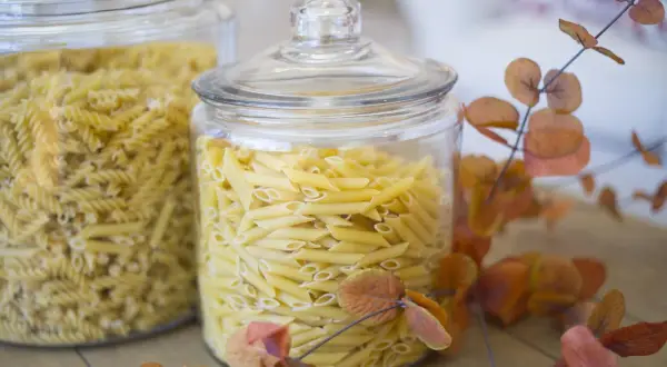 Zwei Glasbehälter voller Nudeln, Penne und Spiralen. Die Frage "wie lange sind nudeln haltbar" wird durch die frische Optik der ungekochten Pasta beantwortet.