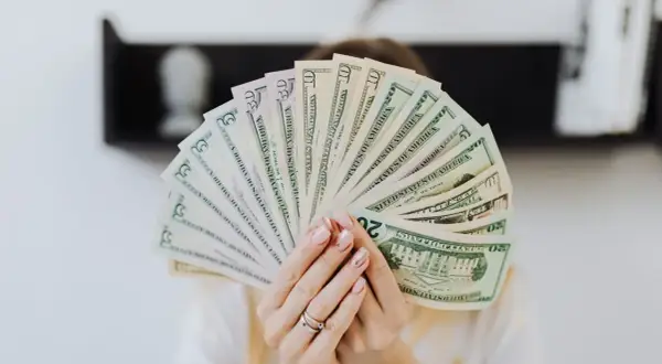 Dłonie trzymają wachlarz banknotów dolarowych. Szukasz firm, kto udziela finansowania firmom bez BIK?