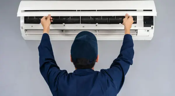 Tecnico con cappellino blu apre il pannello di un condizionatore per manutenzione.