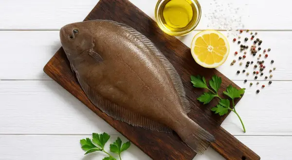 Świeża ryba sola na desce, obok cytryna, oliwa, pieprz i natka pietruszki. Idealna na pyszny obiad.