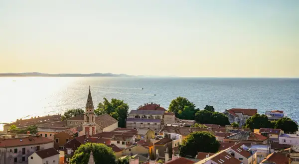 Widok na dachy Zadar i okolice, z kościelną wieżą górującą nad miastem i błękitnym morzem w tle.