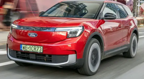 Czerwony Ford Explorer, nowoczesny SUV, pędzi po drodze, odbijając miejski krajobraz w swojej lśniącej karoserii.