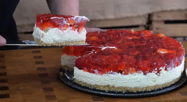 Krojony tort z galaretką truskawkową i bitą śmietaną na spodzie z ciastek.