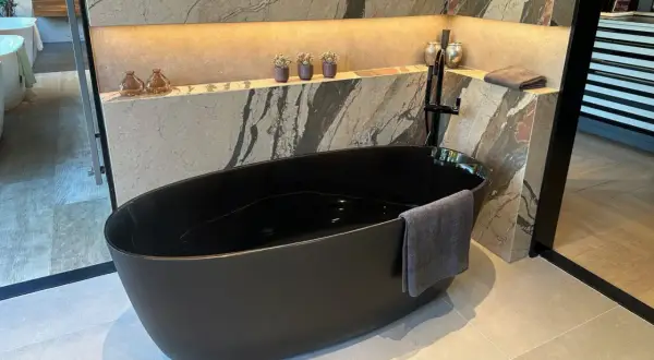 Baignoire noire en acrylique, prête pour un nettoyage. Un drap de bain gris est accroché.