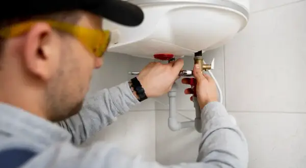 Instalator w okularach ochronnych pokazuje, jak podłączyć bojler elektryczny, pracując przy zaworze.