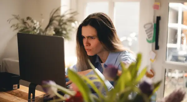 Zmarszczona kobieta przy laptopie, sfrustrowana z powodu braku połączenia z internetem.
