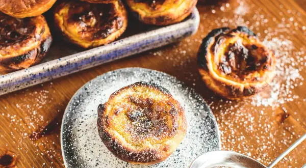 Köstliche, karamellisierte Pastéis de Nata, bestäubt mit Puderzucker, warten auf dem Holztisch.