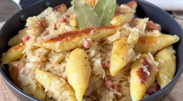 Nudeln mit Sauerkraut und Speck in einer Pfanne, garniert mit Lorbeerblättern.