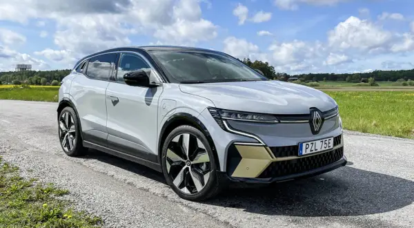 En vit Renault Megane E-Tech står parkerad på en grusväg med en gul och grön fält i bakgrunden. En del av en testkörning.