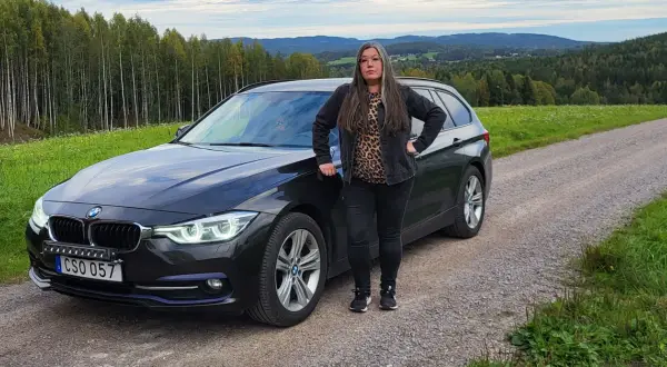 Kvinna vid en svart BMW kombi i svensk landsbygd. Kanske ett bmw b47 problem som gör att hon stannat här.