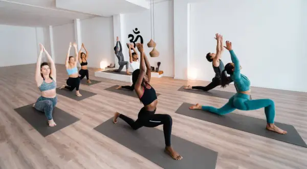 Menschen in einem hellen Raum praktizieren Yoga. Sie sind auf Matten und führen verschiedene Posen aus, was zeigt, dass Yoga Sport ist.