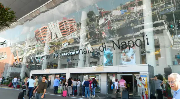 Ludzie z bagażami przed nowoczesnym budynkiem Aeroporto Internazionale di Napoli.