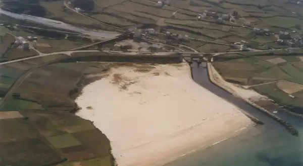 Vista aérea de una playa pampillosa con arena clara, bordeada por un río y campos verdes.