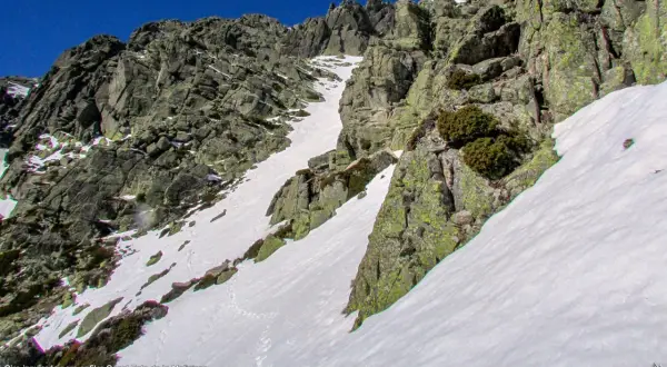 Canal de nieve y roca en la ladera de la Maliciosa, con vegetación escasa y un cielo azul intenso.
