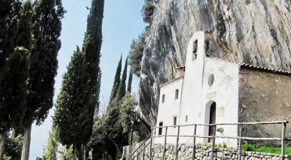 Piccolo eremo di San Valentino incastonato nella roccia, circondato da alti cipressi e un cielo azzurro.