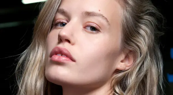 Kobieta z subtelnym makijażem i modnym balejażem na włosach, podkreślającym naturalne piękno.