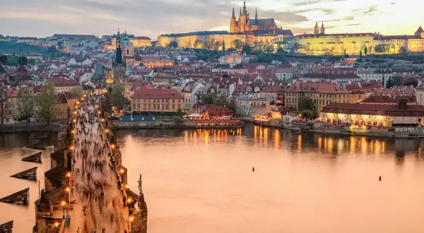 En folktät Karlsbro i Prag vid skymningen, med upplysta byggnader och Pragborgen i bakgrunden. En klassisk vy att se i Prag.